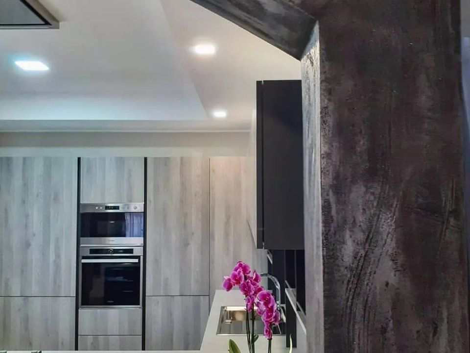 Cucina moderna con mobili in legno chiaro, forno a incasso e un'orchidea rosa sul bancone.