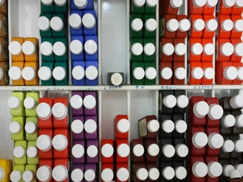 Barattoli di vernice colorata impilati e disposti in file su degli scaffali, etichettati per gruppi di colore.