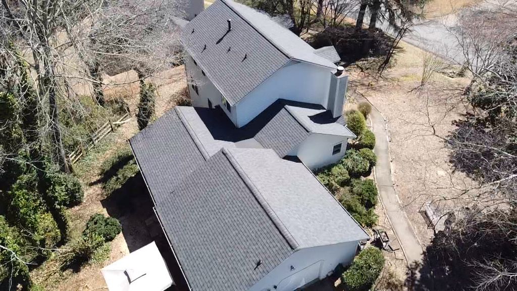 An aerial view of a white house with a black roof surrounded by trees.