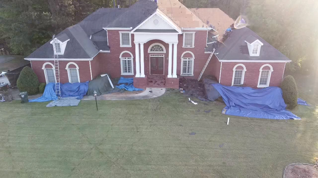 An aerial view of a large brick house covered in tarps.