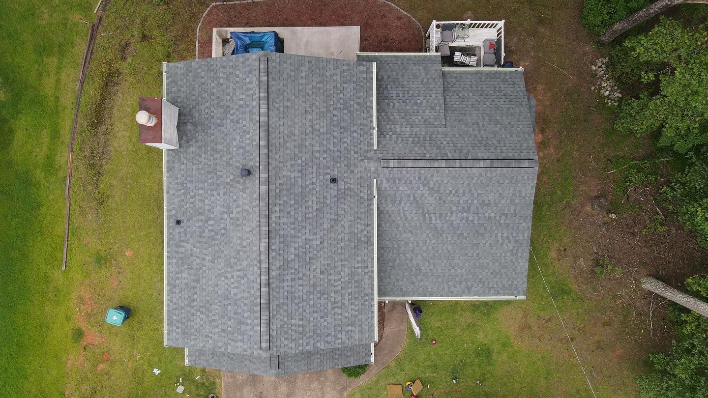 An aerial view of a house with a gray roof surrounded by grass and trees.