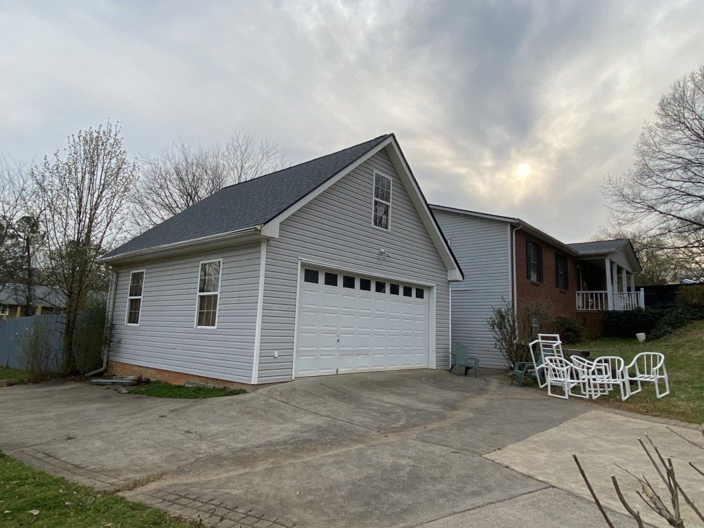 A white garage with a blue roof is next to a brick house.