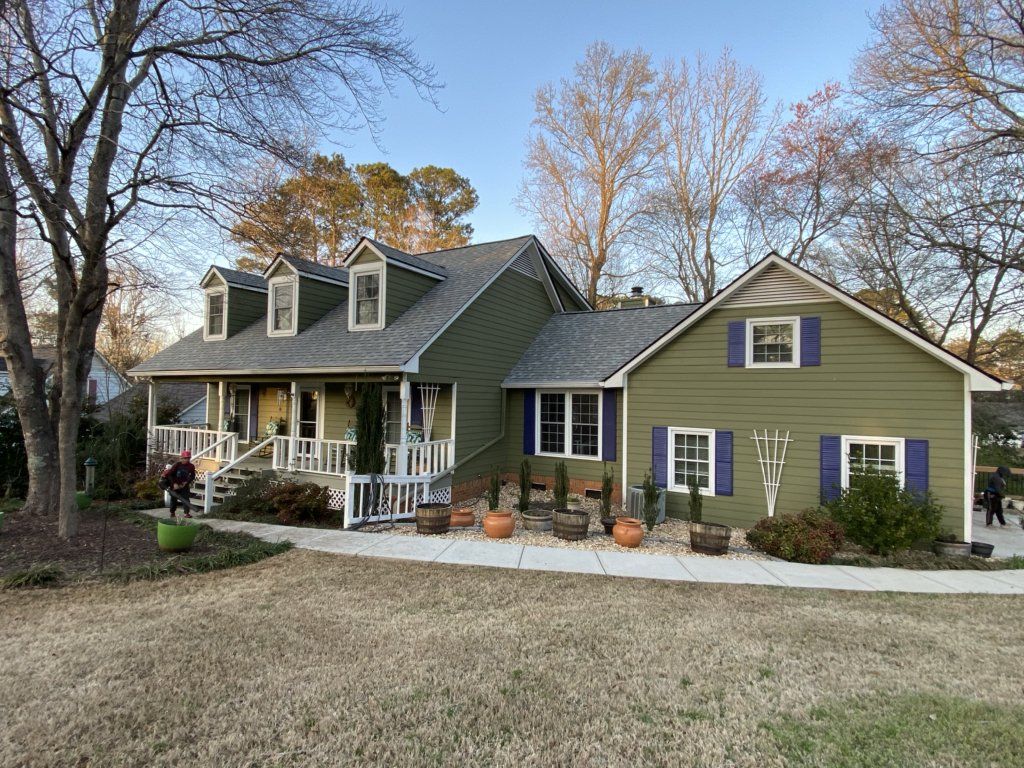 A large green house with blue shutters and a large porch.