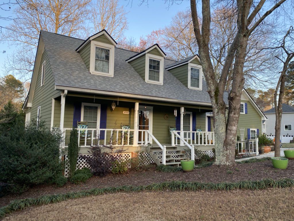 A green house with a gray roof and a large porch.