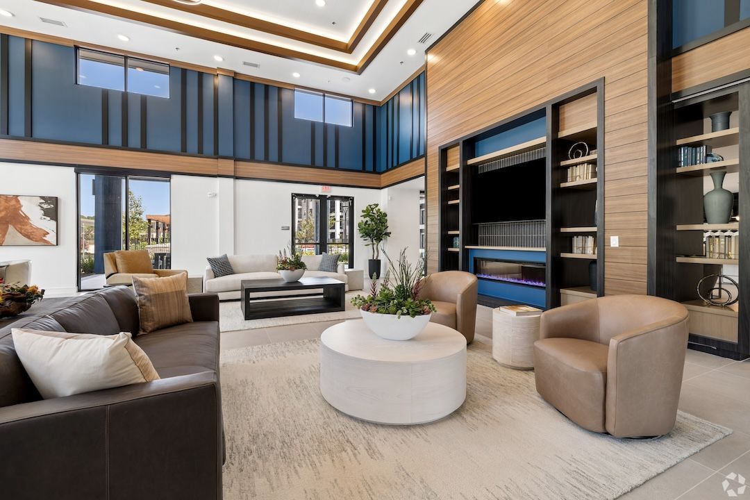 Modern living room with tan seating, round white coffee table, built-in shelves, and large windows
