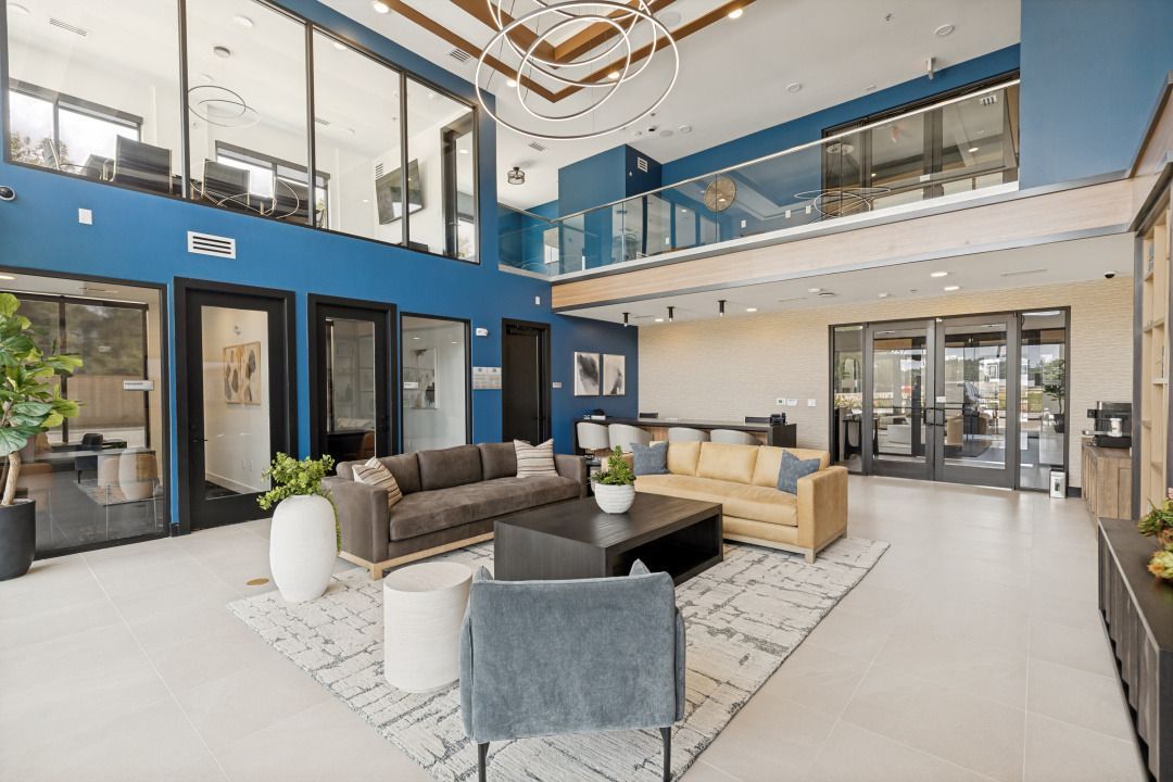 Modern two-story lobby with blue walls, large windows, lounge seating, and a chandelier
