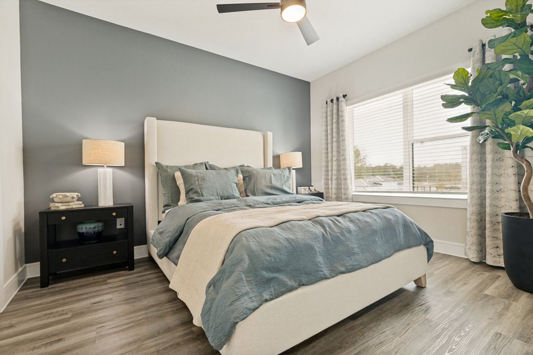 Modern bedroom with a bed, nightstand lamp, large window, and gray-blue decor