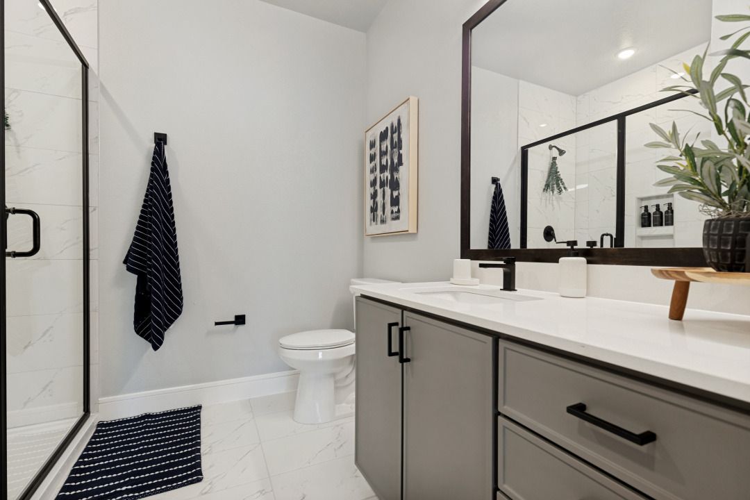 Modern bathroom with gray vanity, white walls, black accents, and a glass shower enclosure