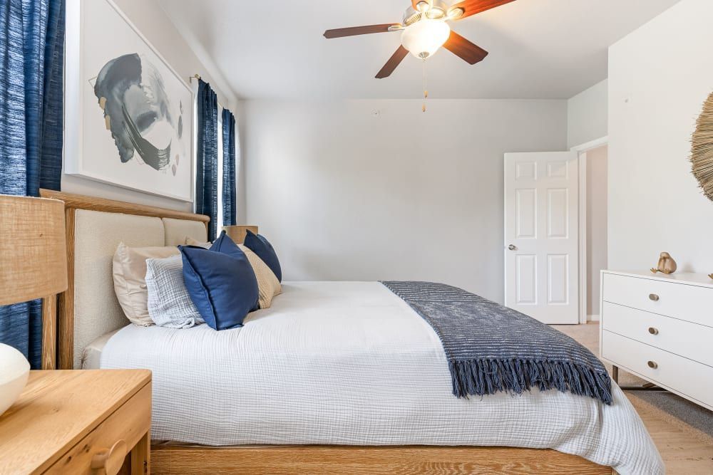 Apartment bedroom with a bed, nightstand, dresser, and ceiling fan at Marquis at Stonegate offers apartments for rent near Benbrook, TX.