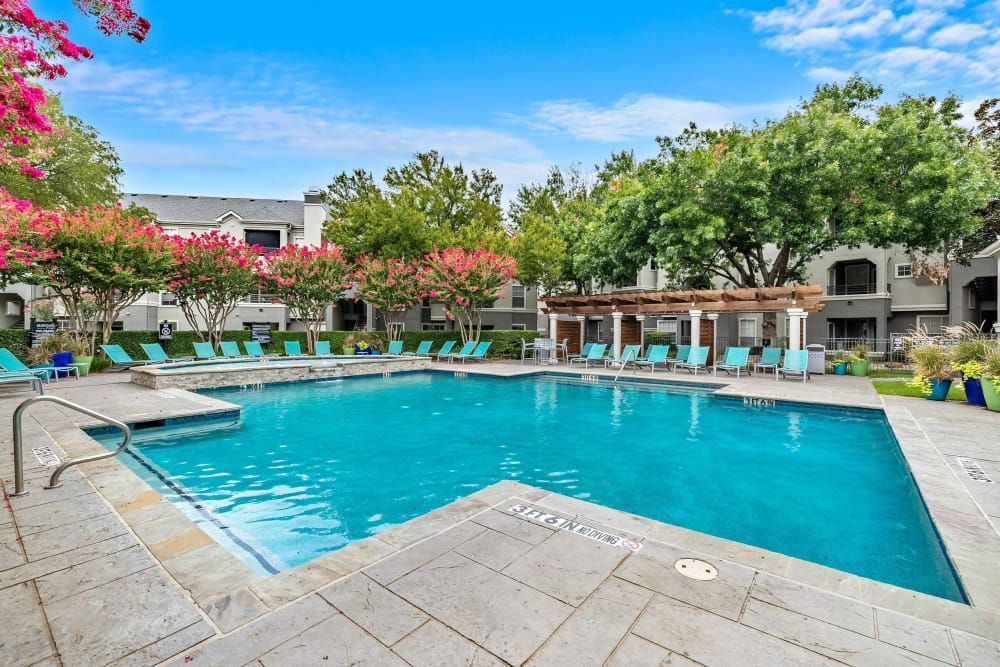 A large swimming pool surrounded by chairs and trees at Marquis at Stonegate offers apartments in Fort Worth, TX.