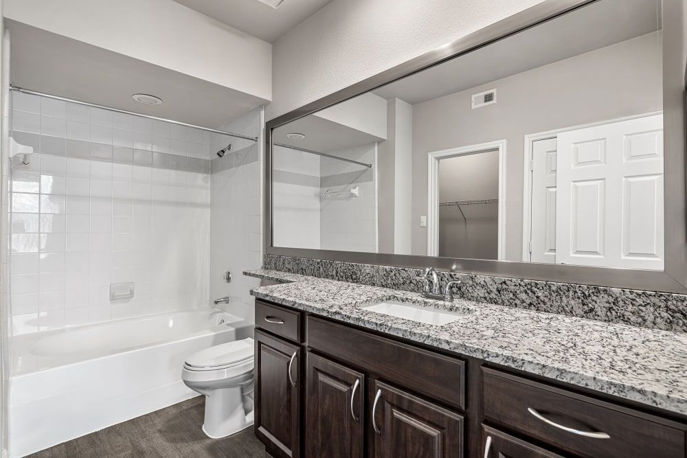 Apartment bathroom with a sink, toilet, bathtub, and large mirror at Marquis at Stonegate offers apartments for rent near Crowley, TX.