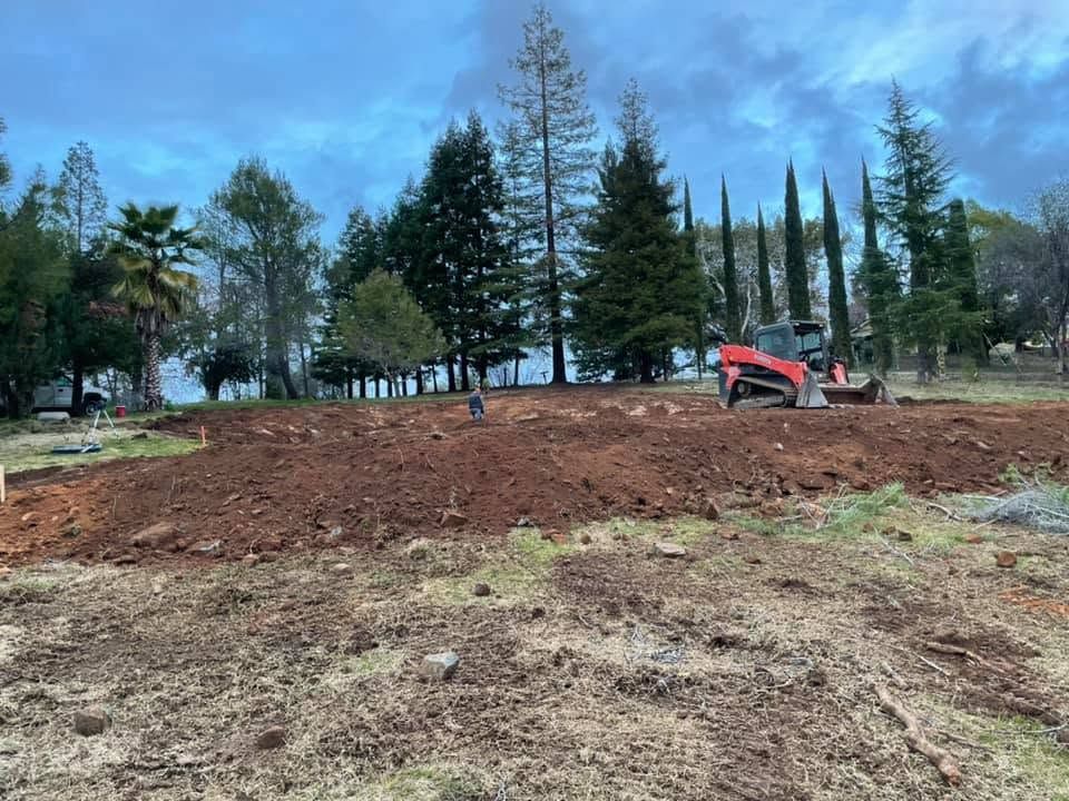 Cleared dirt lot with a red excavator and trees under a blue sky