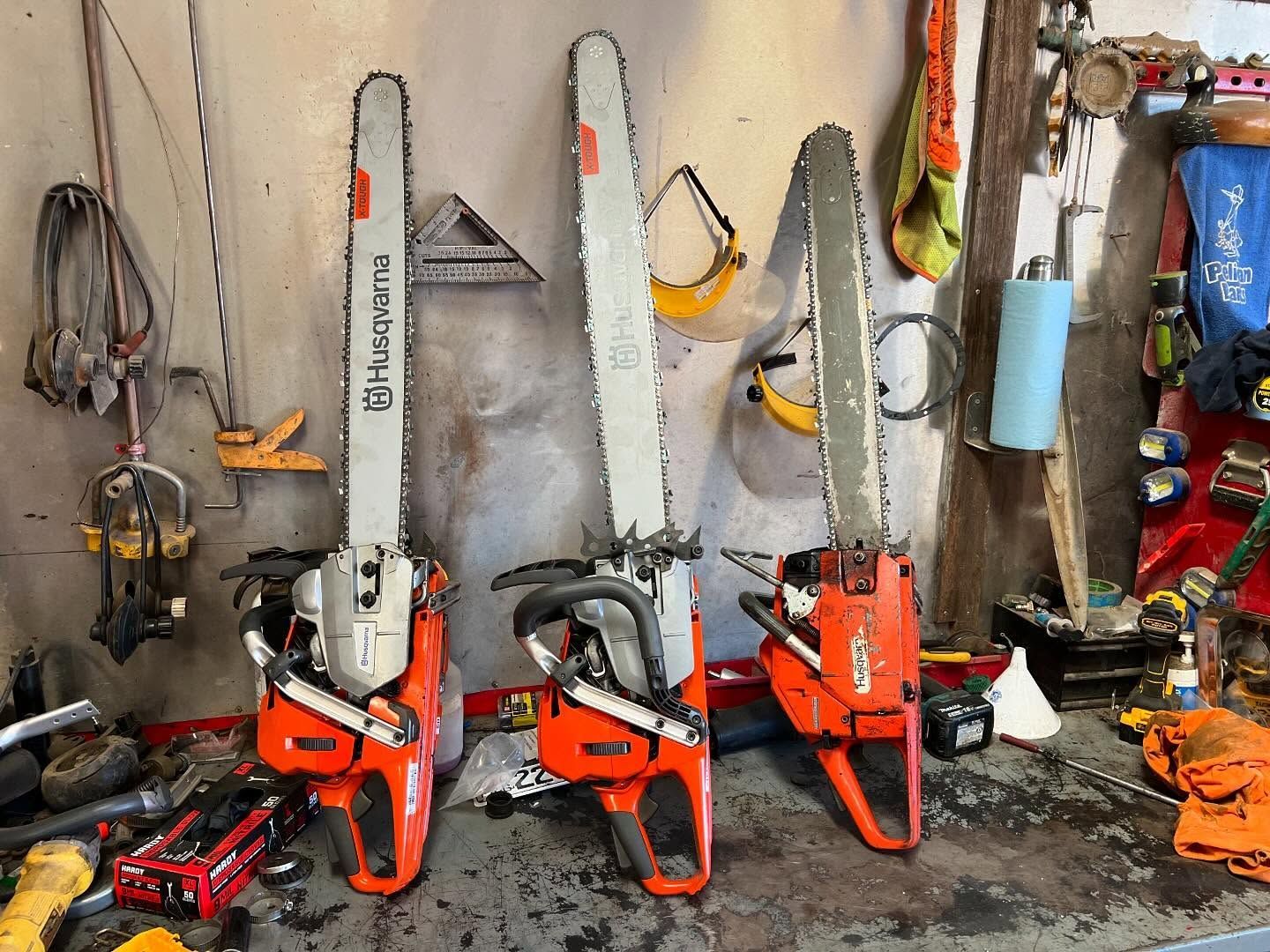 Three orange chainsaws and tools hanging on a workshop wall with assorted equipment below