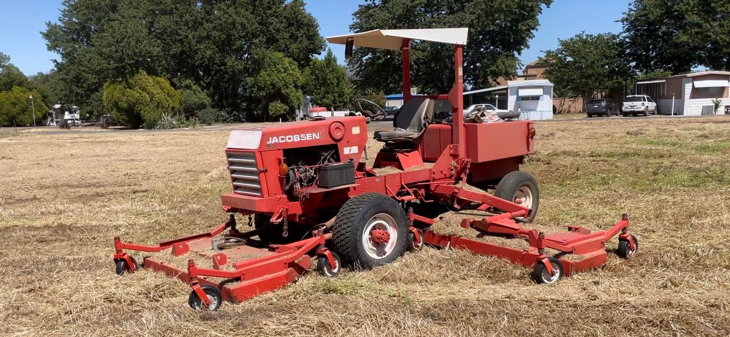 Red farm tractor mowing dry grass in a field