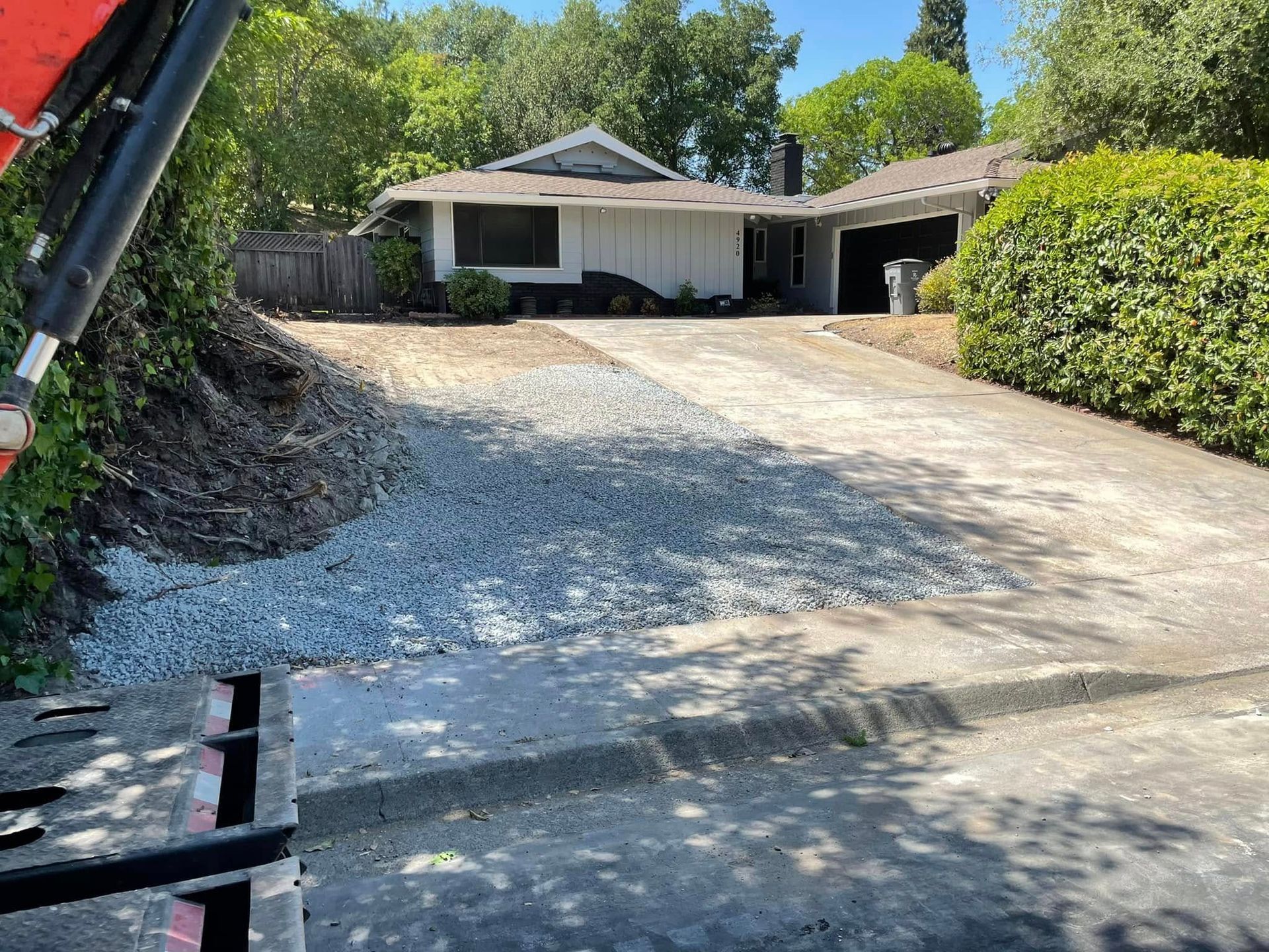 Gravel driveway leading to a house with a carport, bordered by bushes and trees