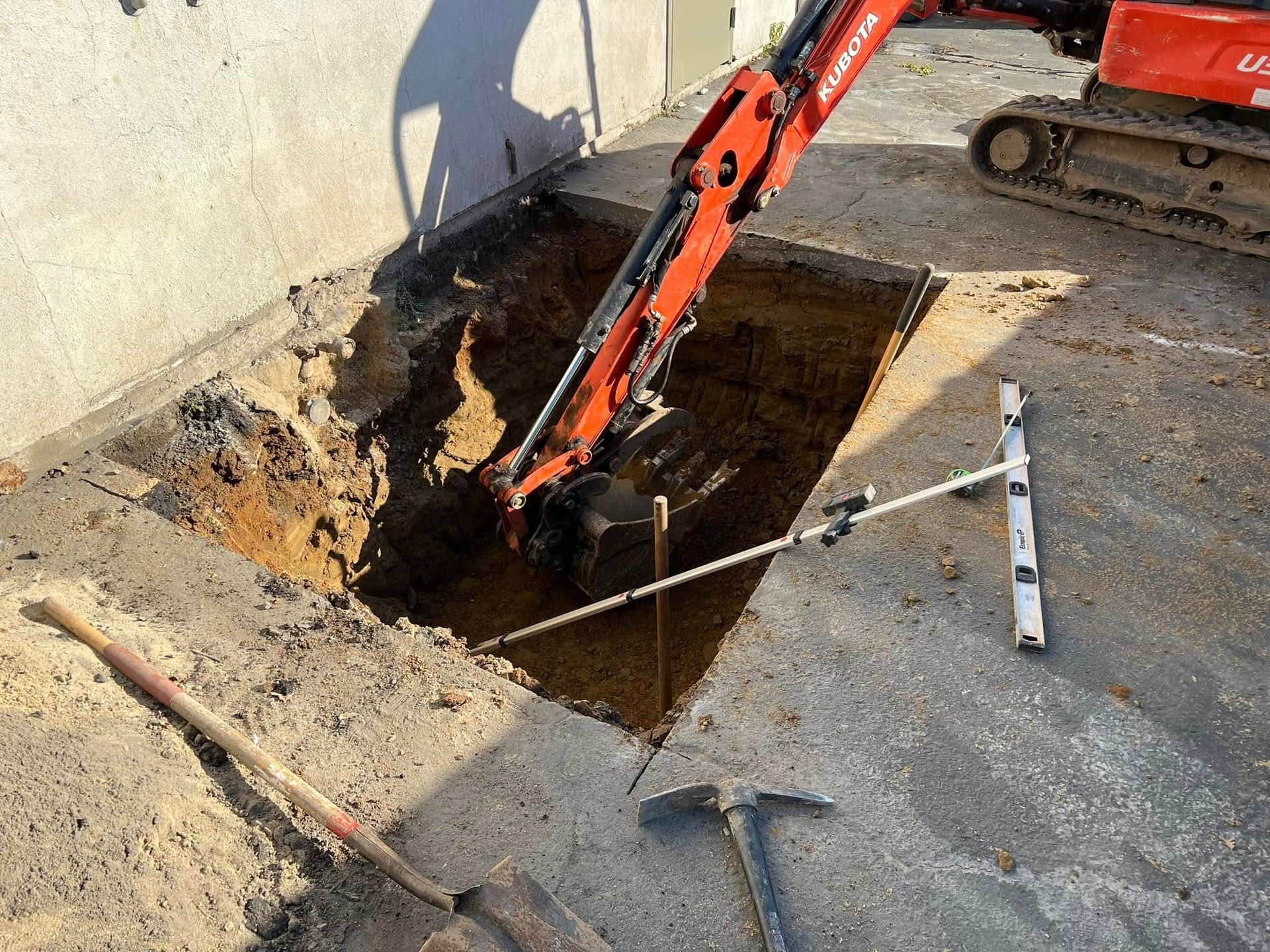 Orange excavator digging a rectangular hole beside a concrete wall on a construction site