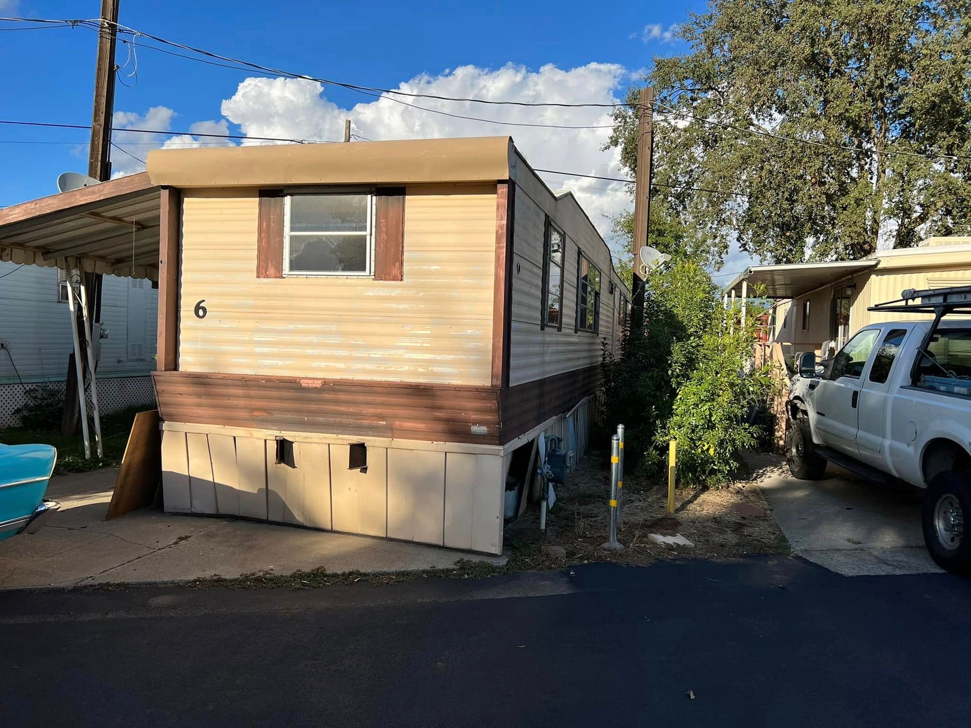Small beige mobile home beside a street, with a white van parked next to it.