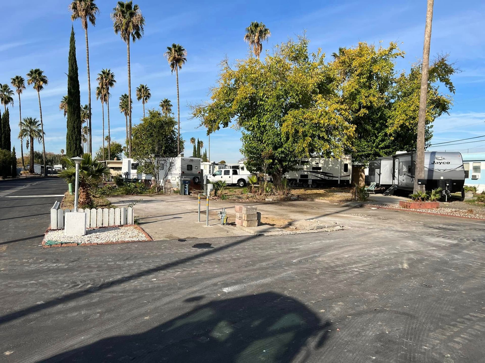 Parking lot with palm trees, a small fenced area, and a white building under a blue sky.