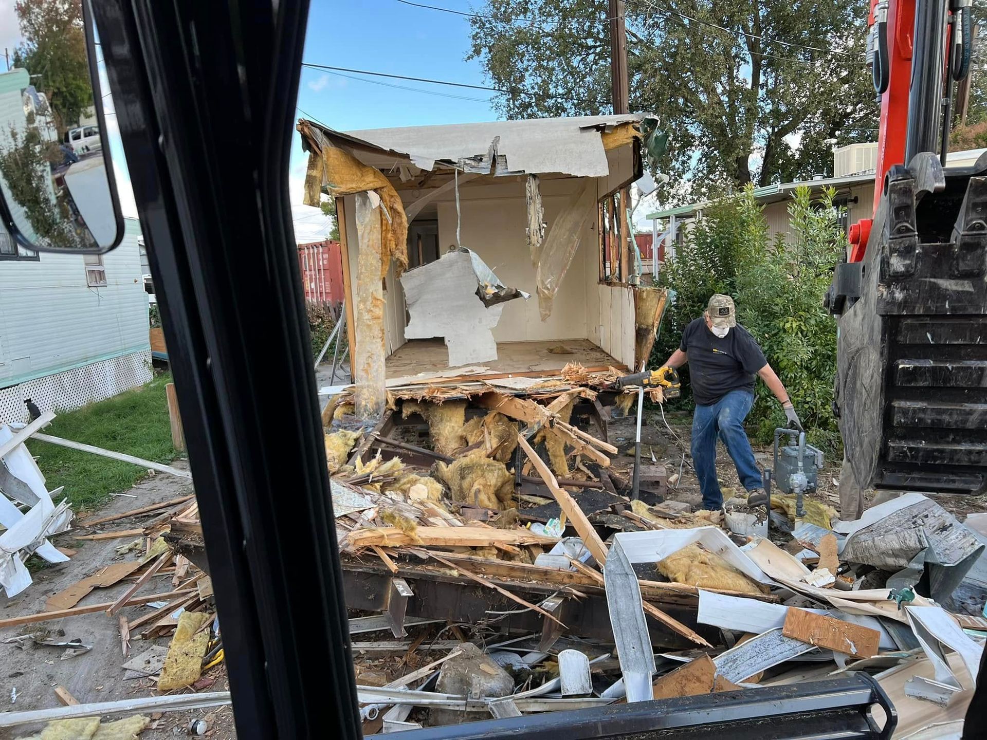 Collapsed house debris beside a road, with a person standing amid wreckage and a vehicle partly visible on the right