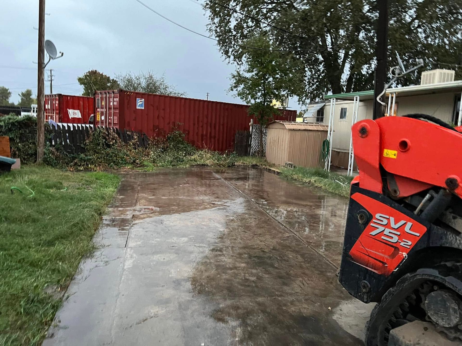 Mud-covered driveway beside a red shipping container, with an orange machine in the foreground.