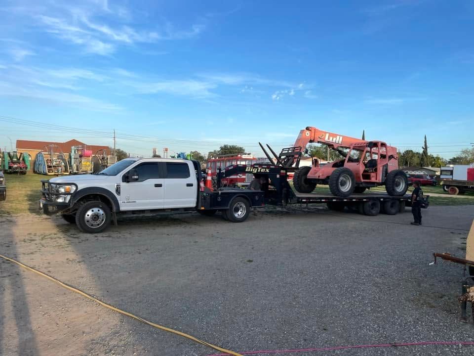 White tow truck hauling a red excavator in a parking lot under a clear blue sky
