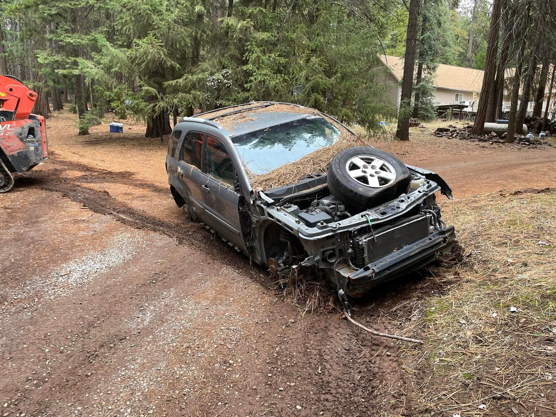 Damaged black SUV off a muddy forest road with front end crushed and spare tire on top