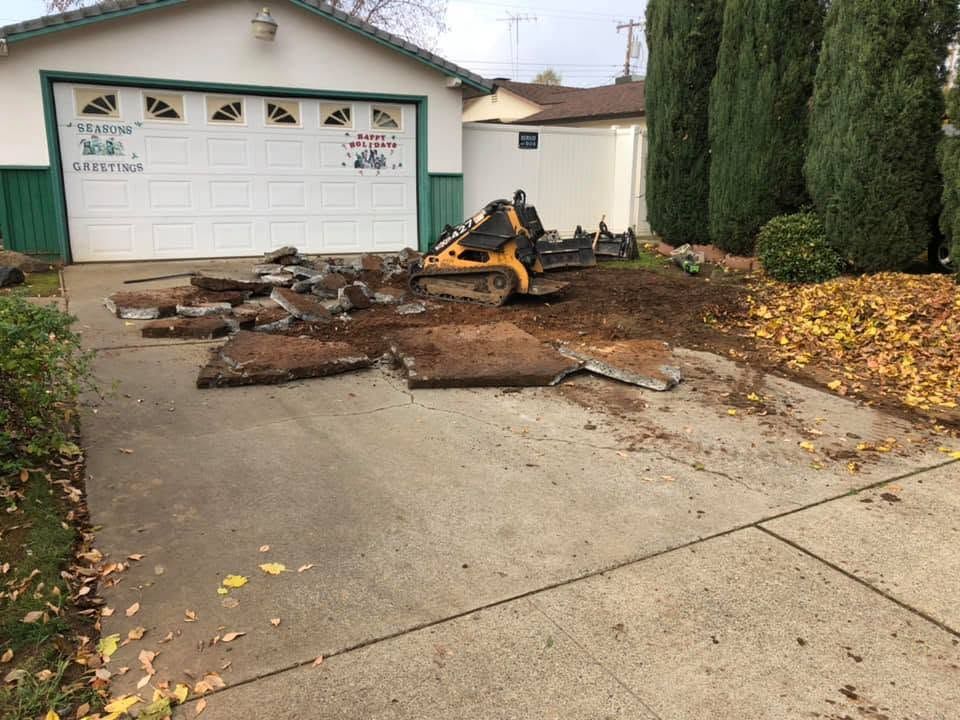 Mini excavator removing debris from a driveway in front of a garage