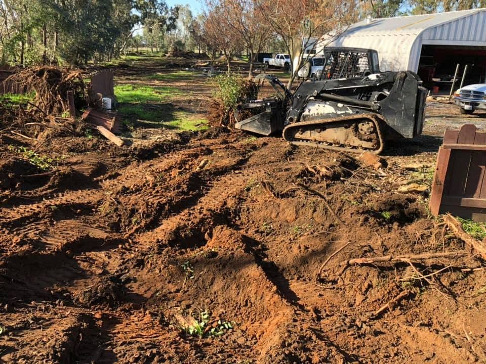 Mud-covered utility vehicle in a debris-strewn yard after damage, with overturned soil and a garage nearby