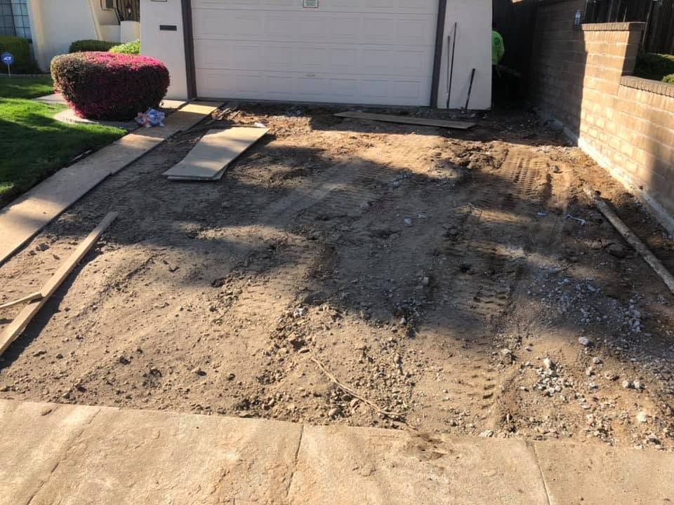 Unpaved driveway area with dirt and gravel leading to a closed garage door and brick wall.