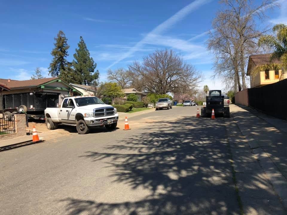 Construction vehicles and orange cones on a residential street under a clear blue sky.