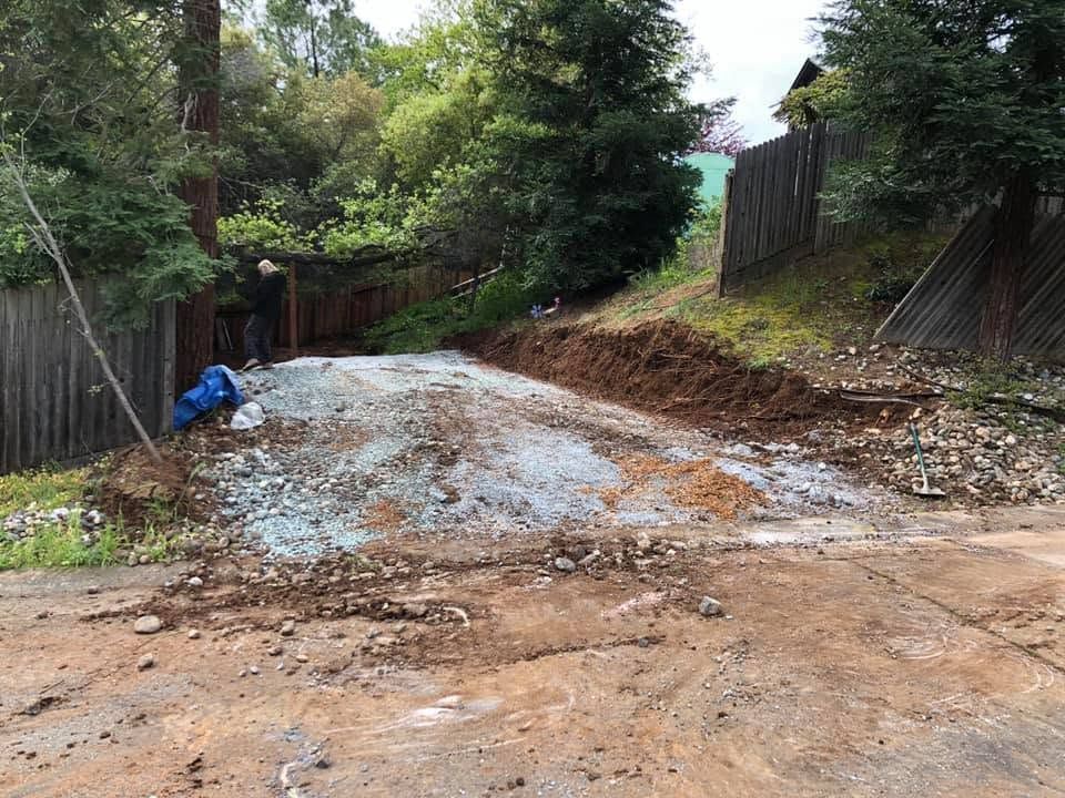 Muddy dirt road with gravel and a blue tarp, bordered by fences and trees on both sides