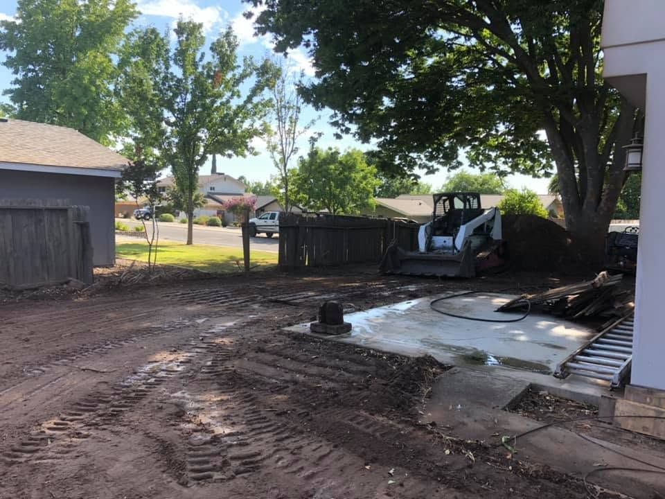 Backyard with muddy ground, damaged concrete, and a skid steer near a fence and trees