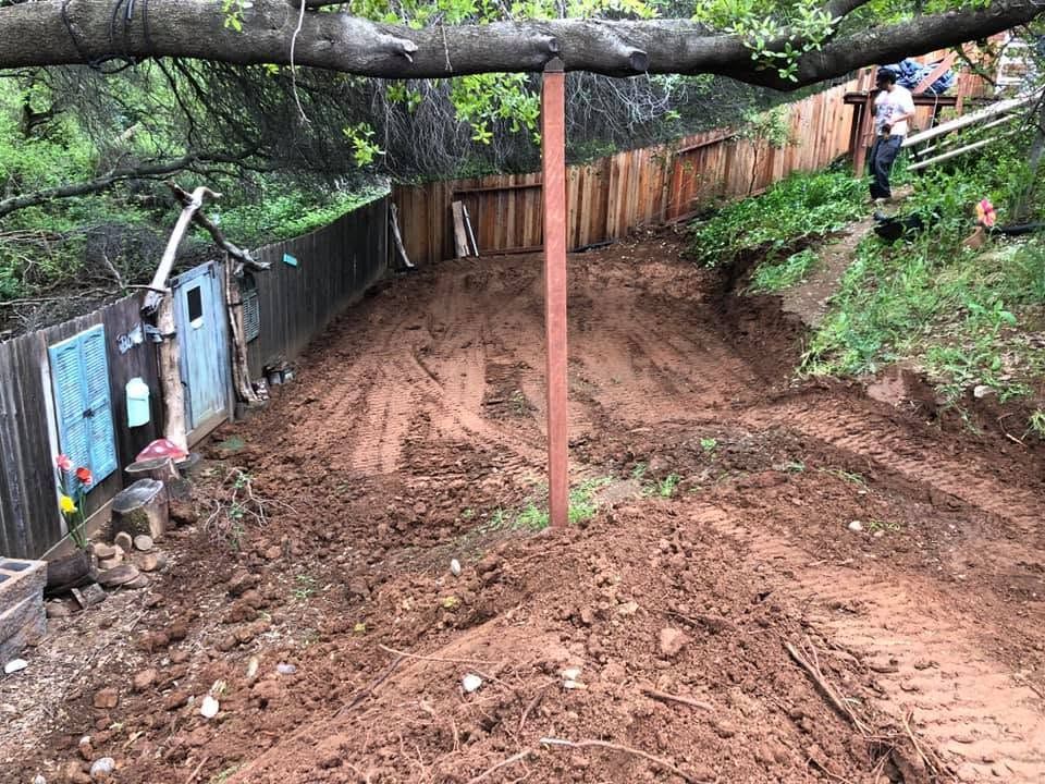 Mud-covered path beside fences and trees, with a fallen branch overhead and a person in the distance.