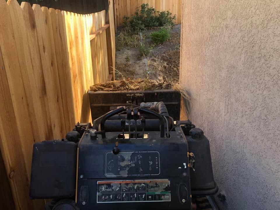 Large black generator in a narrow outdoor passage beside a wooden fence and stucco wall.