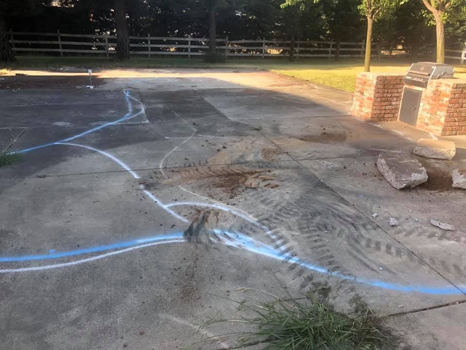 Damaged concrete driveway marked with blue chalk lines and tire tracks near a brick column.