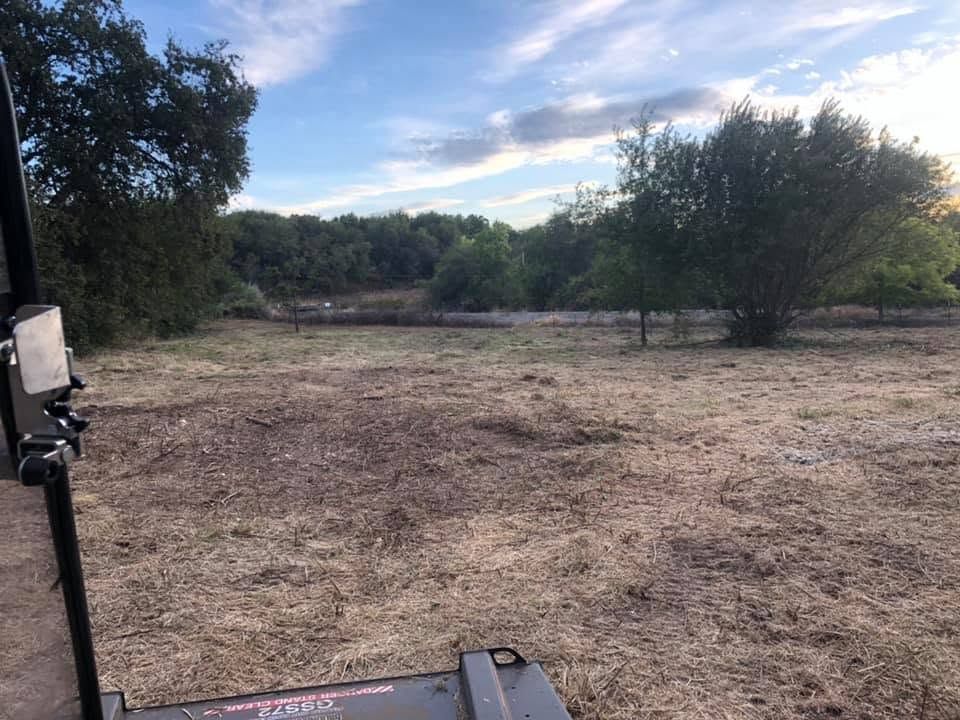 Dry open field with scattered trees under a cloudy sky, viewed from a porch or deck.