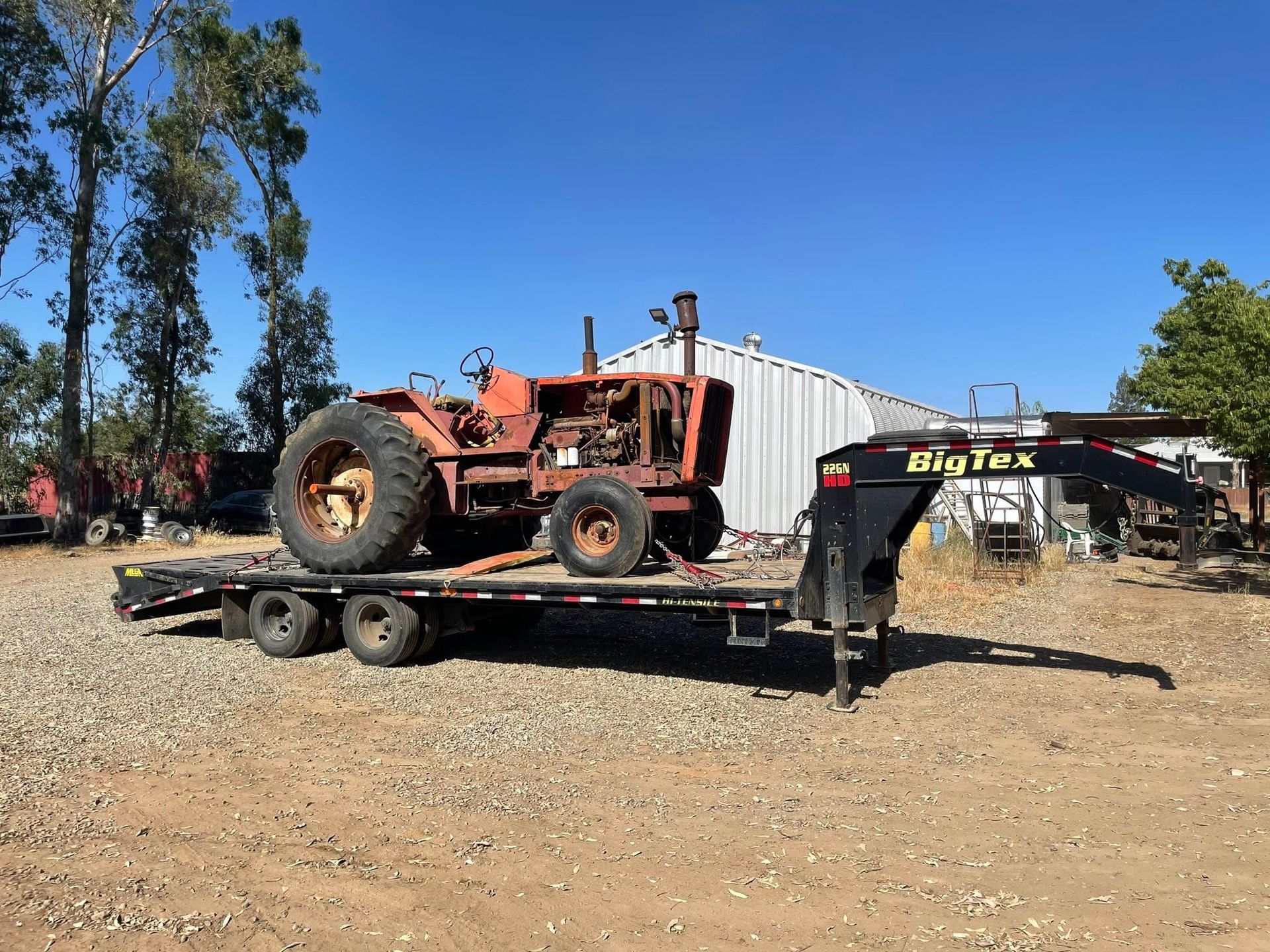 Orange tractor on a flatbed trailer in a gravel yard under a clear blue sky