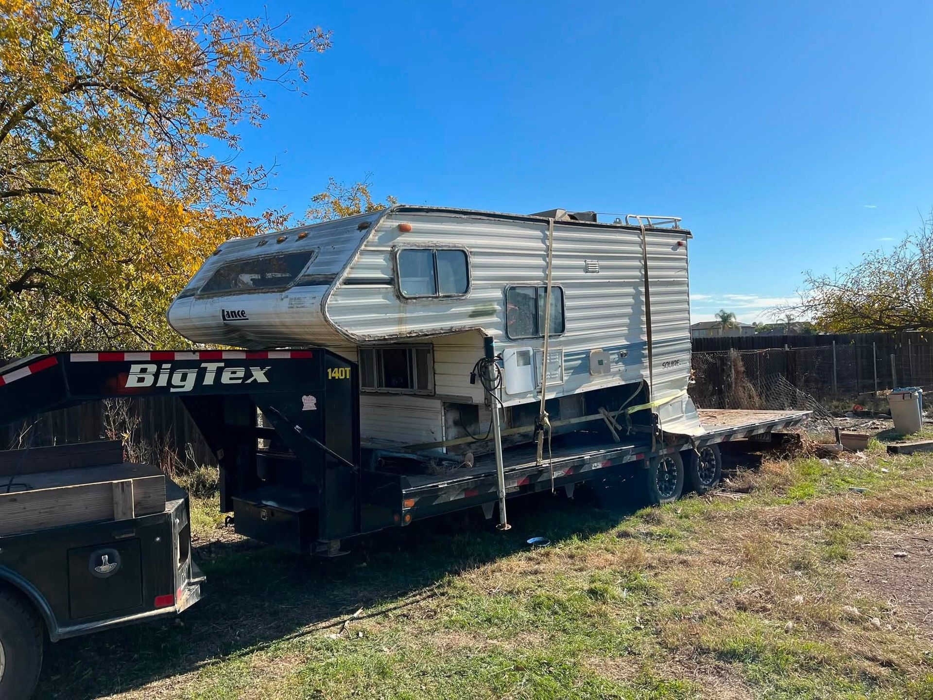 Pickup truck towing a gray camper trailer in a grassy yard under a clear blue sky