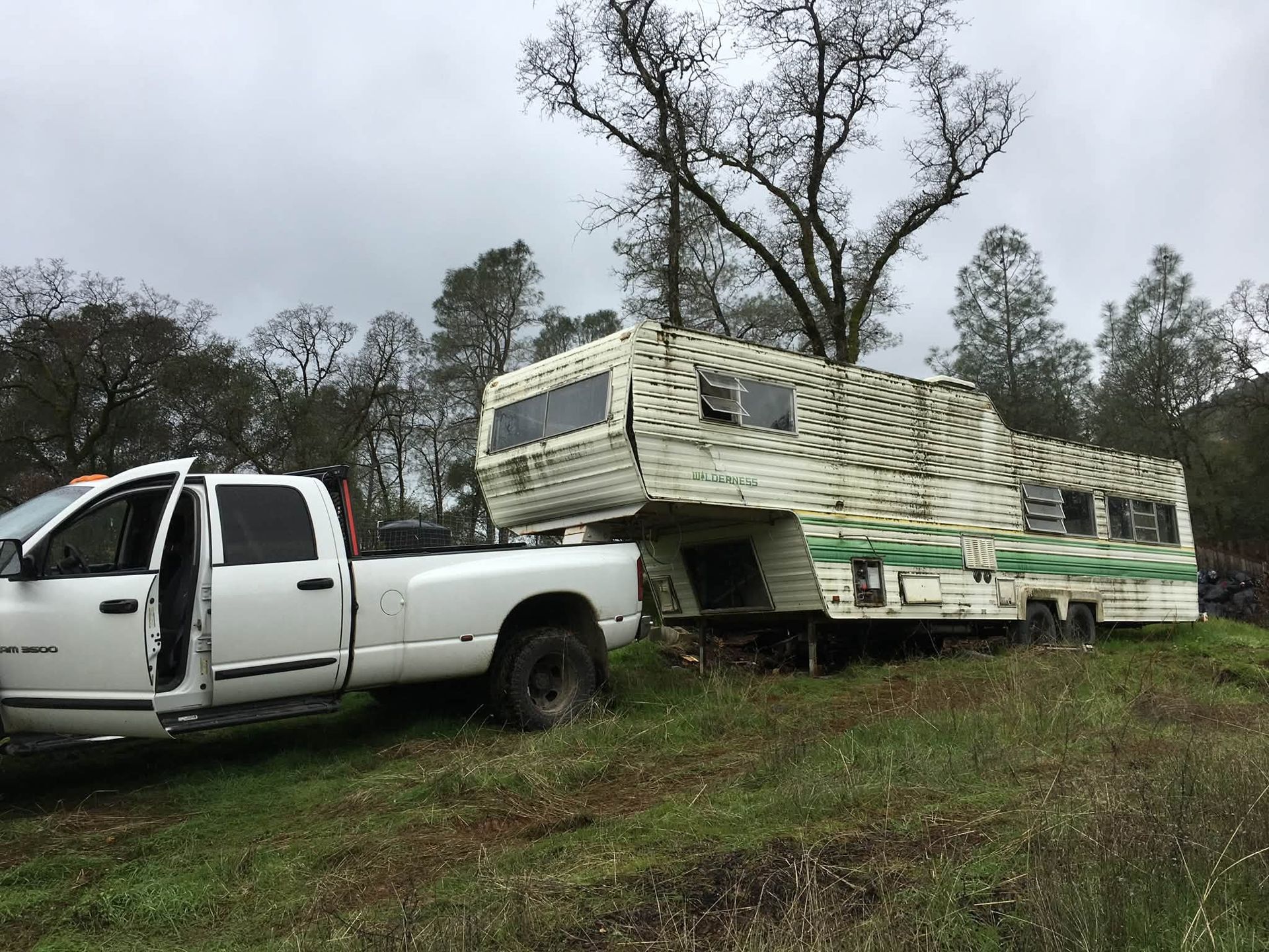 White pickup truck hauling a stacked load of lumber on a grassy slope under cloudy skies