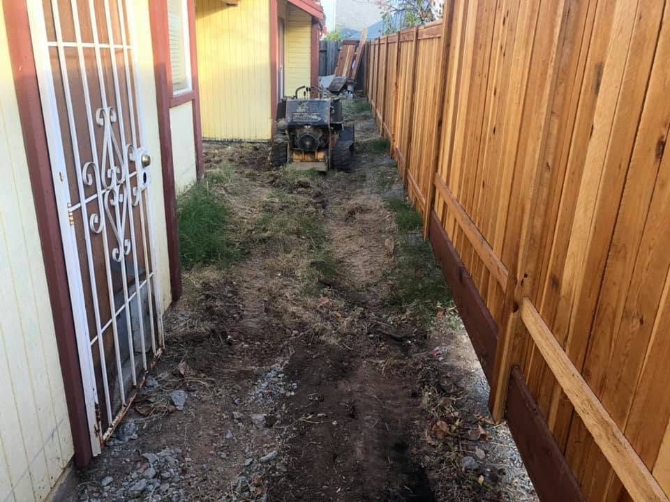 Narrow backyard side yard with a wooden fence, dirt path, and a small utility cart near the end.