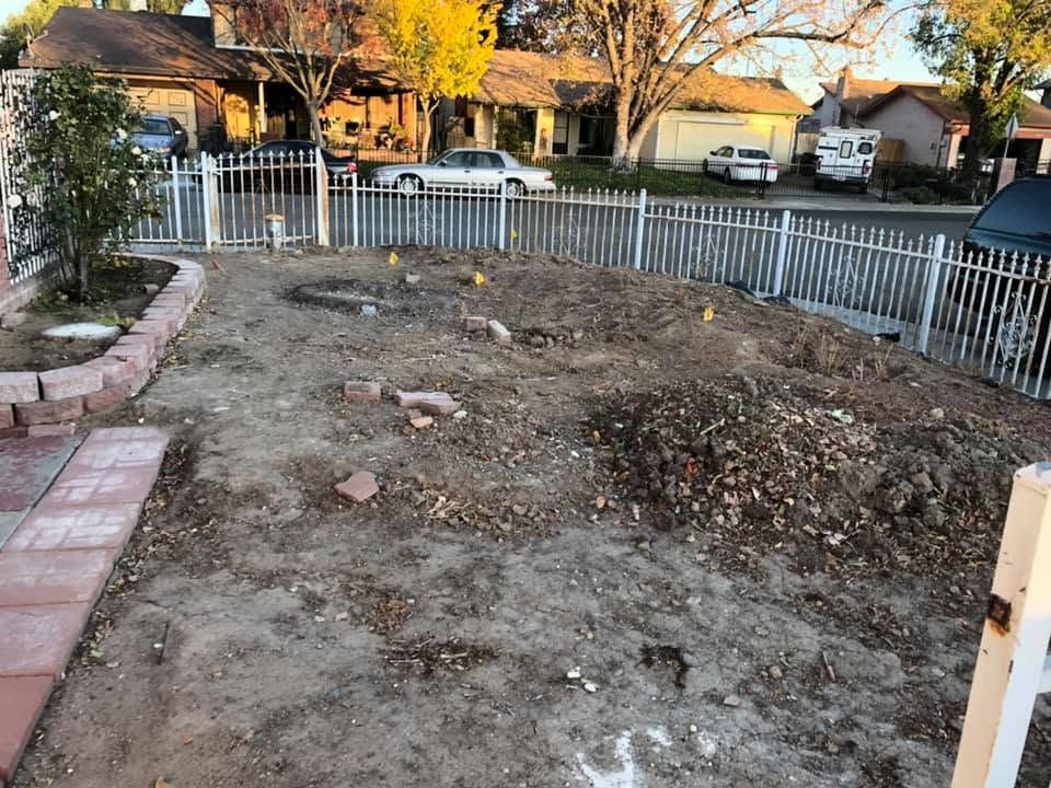 Bare front yard with dirt, rocks, and a white fence in a suburban neighborhood