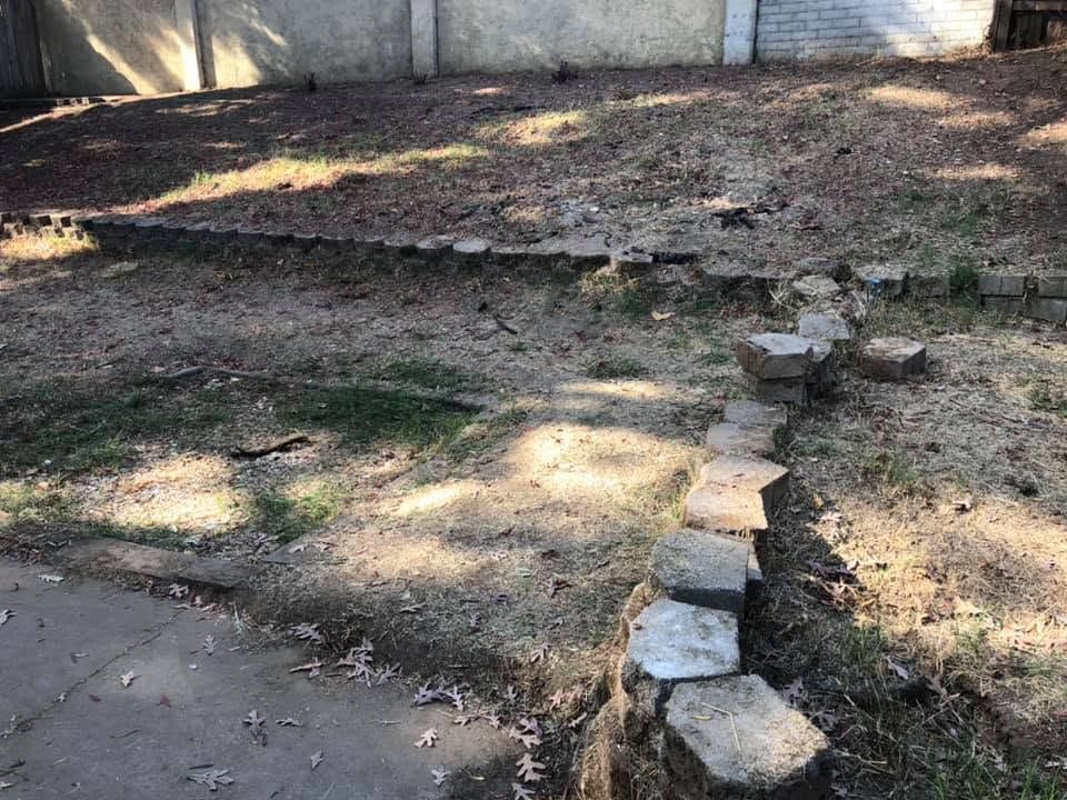 Uneven dirt yard with a row of stepping stones and a concrete path at left
