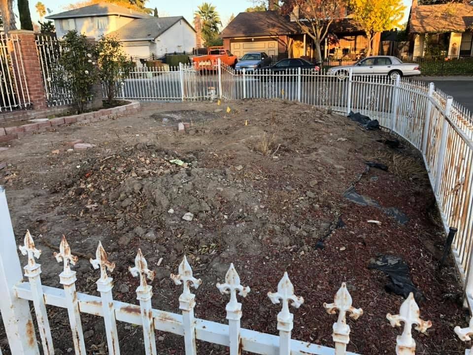 Empty dirt yard enclosed by white metal fences in a suburban neighborhood at sunset