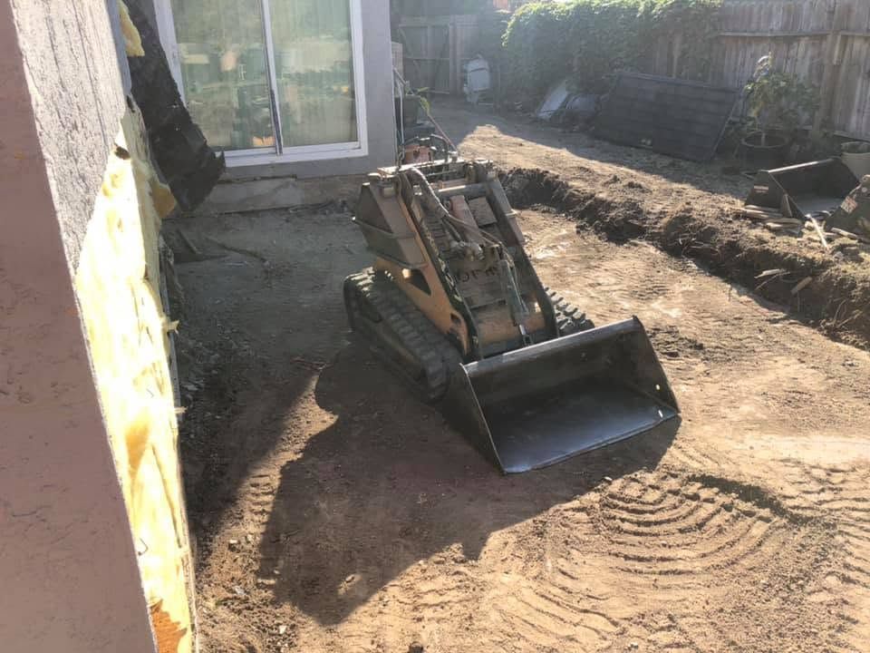 Small front loader parked on a dirt path beside a building, with a shovel bucket raised slightly.