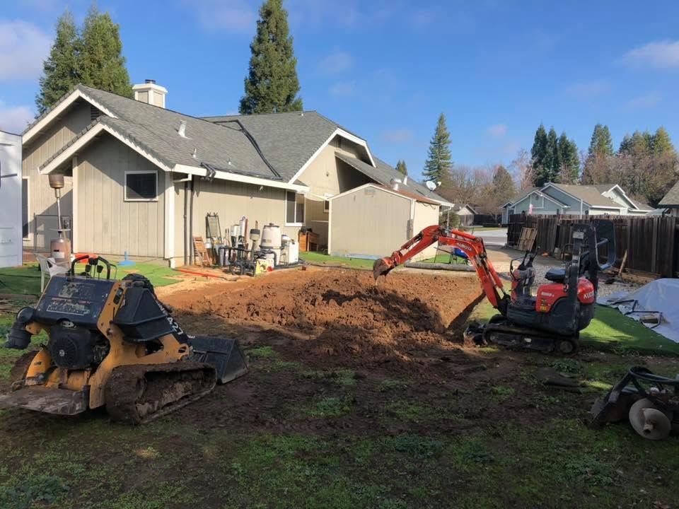Backyard with skid steers and an excavator moving dirt beside a house