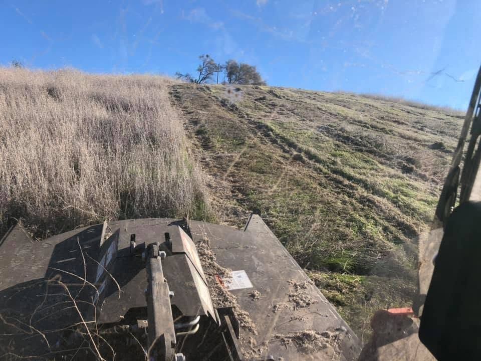 Cab view of a tractor on a dry grassy hillside under a clear blue sky
