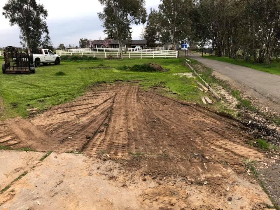 Dirt ramp beside a rural road, with a white truck and fenced field in the background.