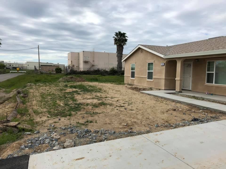 Newly built beige house with a bare dirt front yard and concrete driveway under cloudy skies