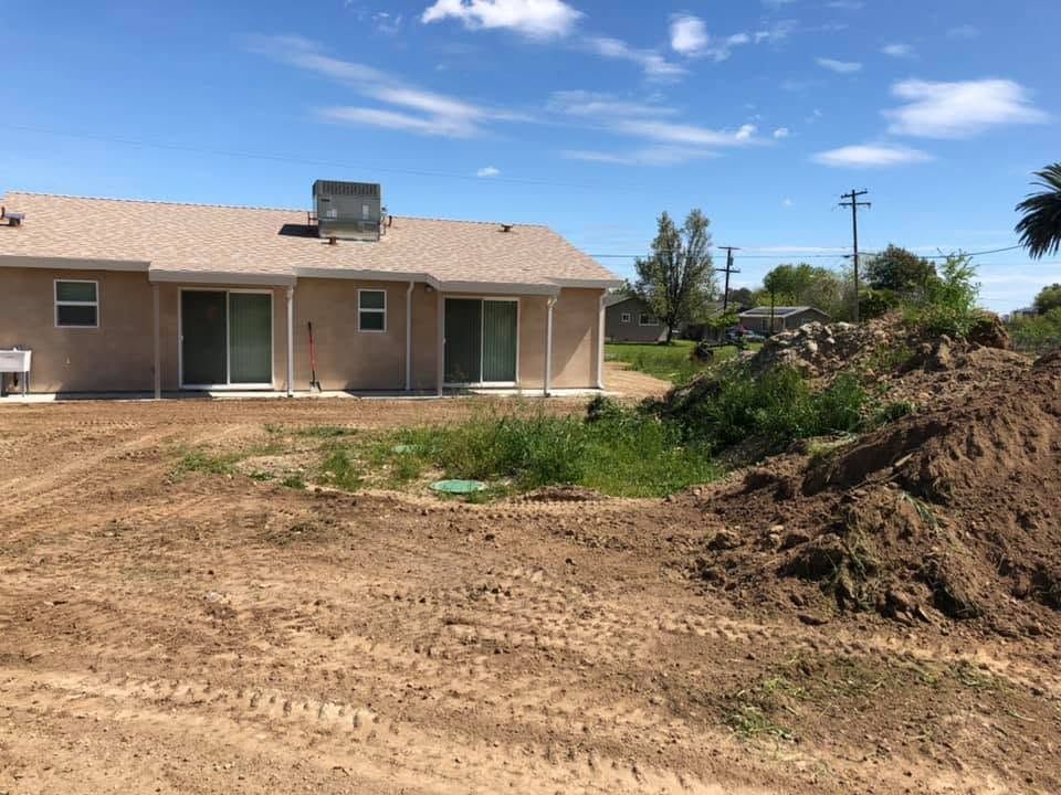Single-story house with dirt yard and construction earth piles under a clear sky