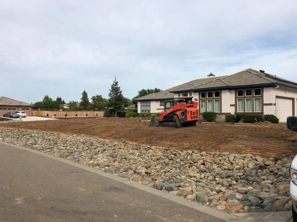 Orange skid steer grading dirt beside a house on a residential construction site